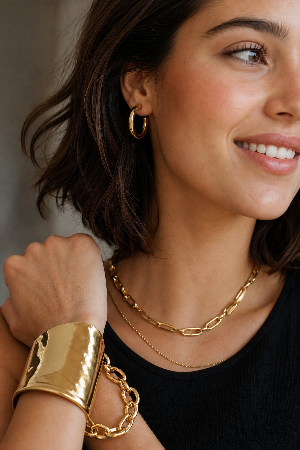 Close-up of a woman in her 20s wearing layered chunky gold-tone jewelry over a black top